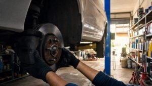 Mecánico con guantes revisando el disco de freno de un auto elevado en un taller mecánico