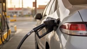 Boquilla de gasolina cargando combustible en un auto plateado en una gasolinera al atardecer