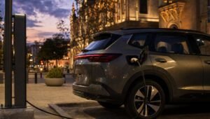 SUV híbrida enchufable conectada a un cargador eléctrico en una plaza urbana al atardecer
