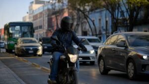 Motociclista con casco integral circulando entre autos en una avenida de una ciudad mexicana