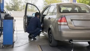 Técnico conectando un escáner de diagnóstico a un auto durante la verificación vehicular, con la sonda de medición en el escape